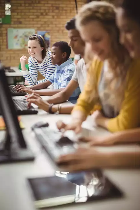 Diverse group of students smiling while working on computers in classroom